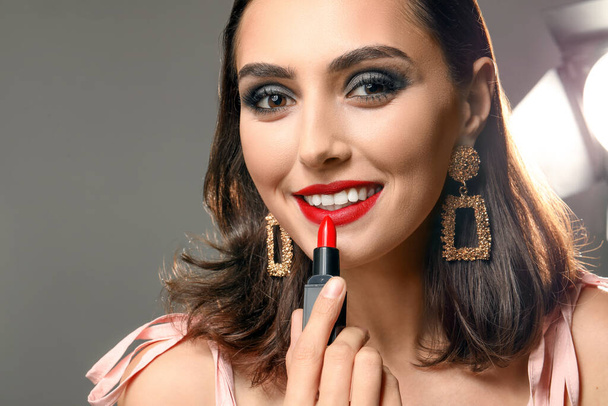 Hermosa mujer joven aplicando maquillaje sobre fondo gris
 - Foto, imagen