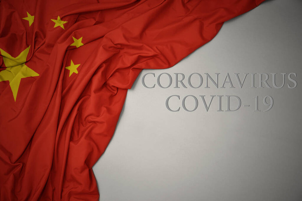 κυματίζει πολύχρωμο εθνική σημαία της Κίνας με κείμενο coronavirus covid-19 σε γκρι φόντο. - Φωτογραφία, εικόνα