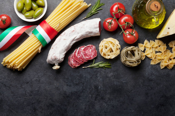 Итальянская кухня ингредиенты. Паста, сыр, салями, оливки и помидоры. Плоский вид сверху лежал на каменном столе с копировальным пространством - Фото, изображение