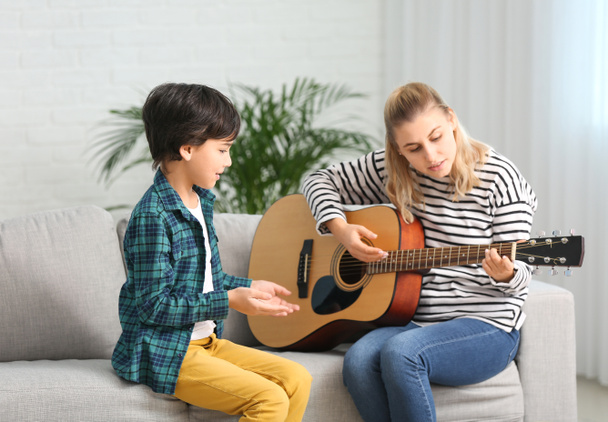 Частный учитель музыки дает уроки гитары маленькому мальчику дома
 - Фото, изображение