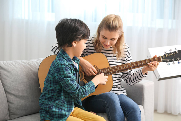 Ιδιωτικός δάσκαλος μουσικής δίνει μαθήματα κιθάρας σε μικρό αγόρι στο σπίτι - Φωτογραφία, εικόνα
