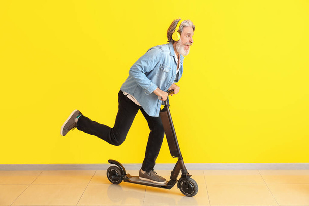 Felice uomo anziano con calcio scooter e cuffie vicino alla parete di colore
 - Foto, immagini