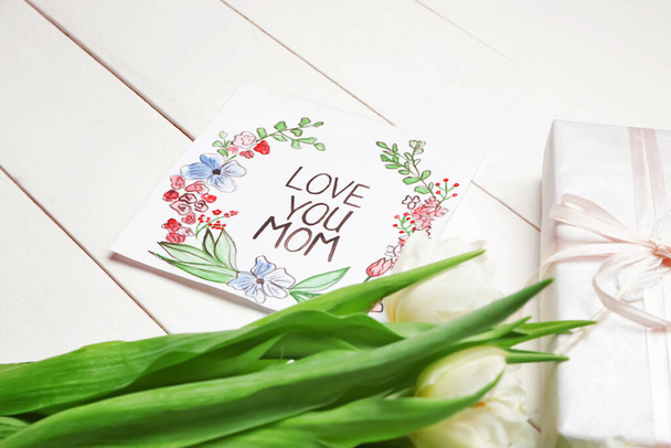 Bukiet pięknych kwiatów, kartka i prezent na Dzień Matki na białym drewnianym tle - Zdjęcie, obraz