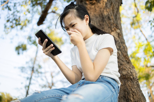 Smutna azjatycka studentka ofiara cybernękania online samotnie siedząca w szkole na świeżym powietrzu, nastolatka odbierająca SMS-y przez telefon komórkowy, molestowana, nękana, wystraszona i zdesperowana  - Zdjęcie, obraz