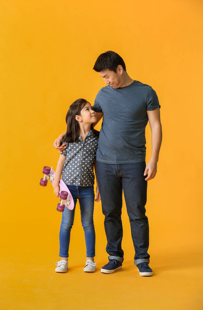 Happy Asian man and his little daughter with skateboard on color background - Photo, Image