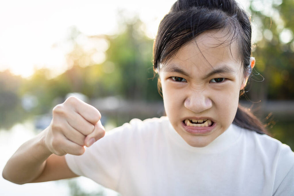 Серьёзная азиатская девочка с поднятым кулаком для предупреждения об угрозах или ссоры, злая женщина, угрожающая кулаком, вот-вот ударит, агрессивная школьница, выражение лица, концепция агрессии, хулиган
  - Фото, изображение