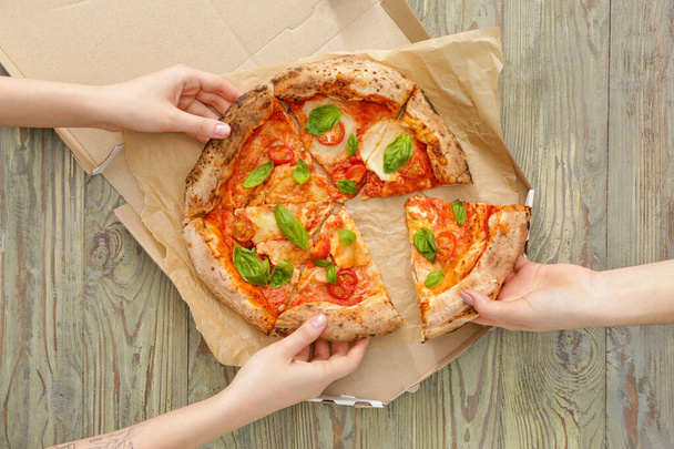 Ihmiset ottavat viipaleita herkullista pizzaa Margherita pöydästä
 - Valokuva, kuva