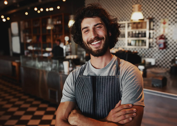 Portrait of smiling handsome young waiter standing at coffee shop - Foto, Imagem