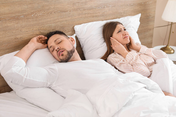Νεαρή εκνευρισμένη γυναίκα στο κρεβάτι με σύζυγο που ροχαλίζει στο σπίτι - Φωτογραφία, εικόνα