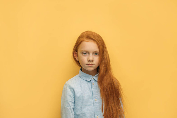 retrato de menina criança de cabelos vermelhos grave isolado sobre fundo amarelo
 - Foto, Imagem