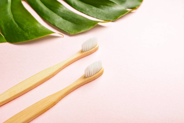 Houten tandenborstels met tropisch blad op kleur achtergrond - Foto, afbeelding