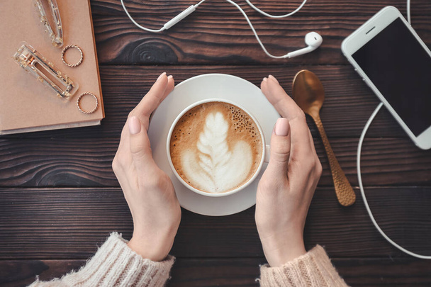 Egy nő finom cappuccinót iszik a fa asztalnál. - Fotó, kép