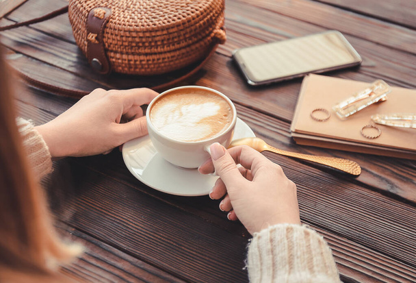 Vrouw die lekkere cappuccino drinkt aan houten tafel - Foto, afbeelding