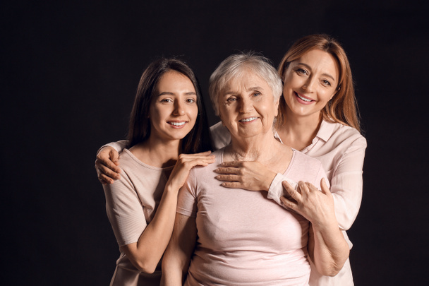 Portrait of mature woman with her adult daughter and mother on dark background - Photo, Image