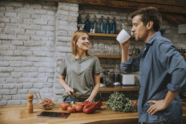 Young  woman cooking while man drinking coffee  in the rustic kitchen - Photo, Image