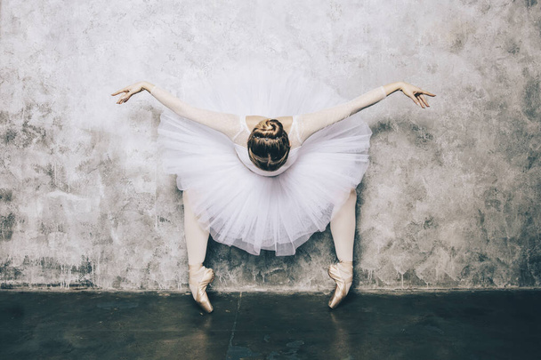Молодая балерина в белом платье с идеальным телом танцует против деревенской стены
 - Фото, изображение