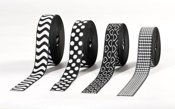 Cuatro rollos de bandas elásticas estampadas en blanco y negro que se muestran en el extremo sobre blanco con corazones, lunares, rayas en zigzag y diseños de arenque para su uso en la industria de la moda
 - Foto, imagen