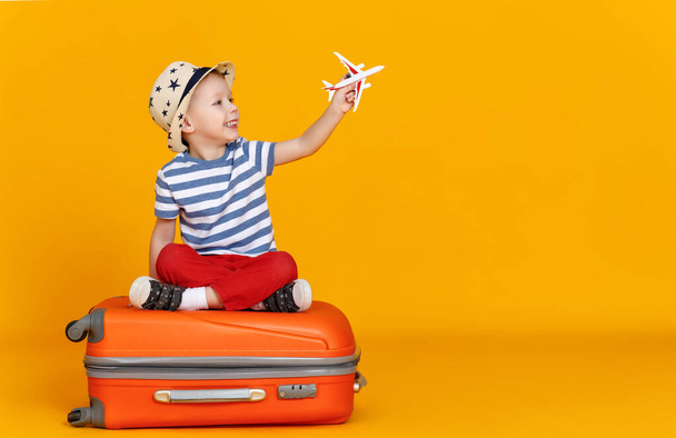 Joyeux petit garçon avec avion jouet assis jambes croisées contre backgroun jaune
 - Photo, image