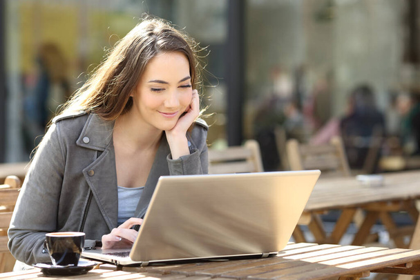Young satisfied girl watching media content on her laptop on a cafe terrace a sunny day - Foto, Bild