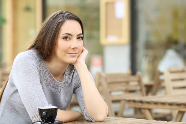 Retrato de una hermosa joven mujer seria mirando a la cámara sentada en una terraza del café
 - Foto, Imagen