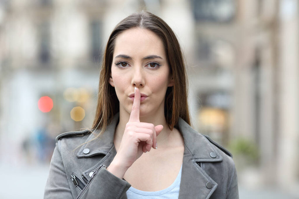 Front view portrait of serious woman asking for silence with finger on lips on city street - Foto, imagen