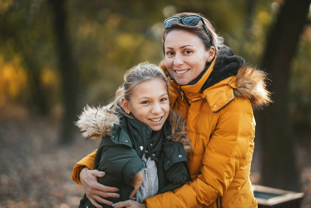 Schöne Mutter und ihre glückliche Teenager-Tochter amüsieren sich im Park, umarmen sich und lächeln. - Foto, Bild