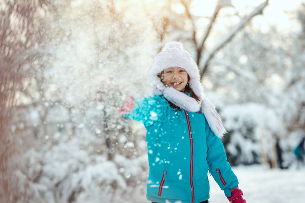 Cute little happy girl in winter clothes is having fun in snowy winter day. - Photo, Image