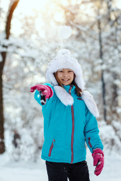 Χαριτωμένο μικρό χαρούμενο κορίτσι με χειμωνιάτικα ρούχα διασκεδάζει σε χιονισμένη χειμωνιάτικη μέρα. - Φωτογραφία, εικόνα