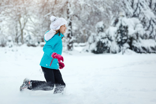 Cute little happy girl in winter clothes is having fun running in snowy winter day. - Фото, изображение