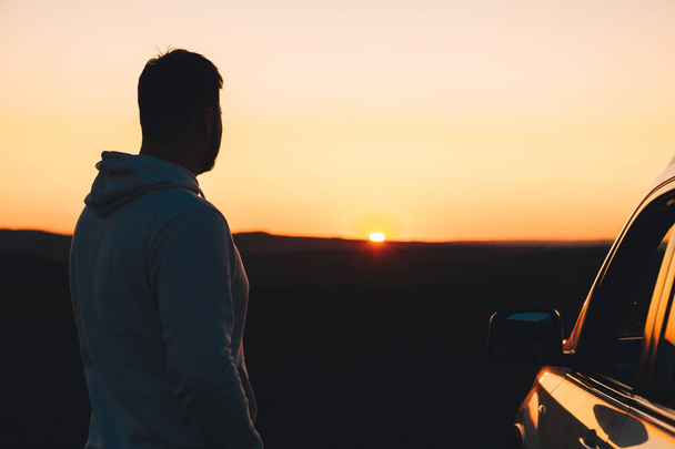 hombre de pie cerca de coche suv blanco mirando el espacio de copia puesta del sol - Foto, imagen