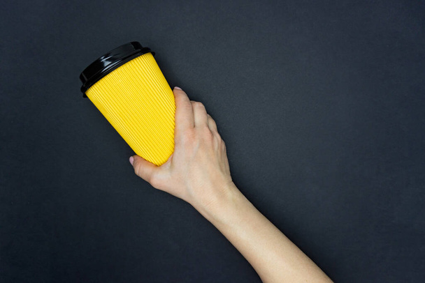 Yellow coffee paper cup in female hand is on yellow background - Фото, изображение