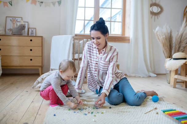 Young mom and daughter playing with artificial stones on the floor - Photo, image