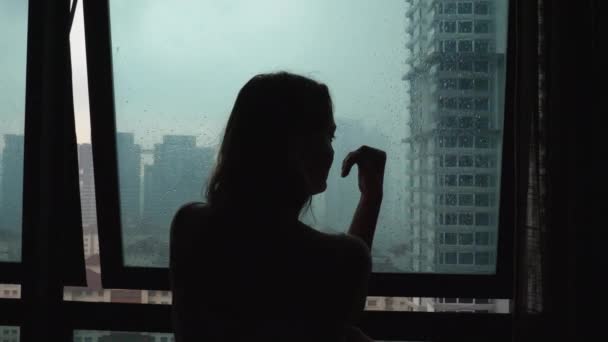 Silhouette sad loneliness woman touch glass window at rain day - Materiał filmowy, wideo