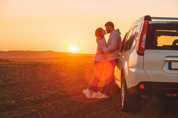 Romantik an çifti gün batımında beyaz SUV arabasının yakınında öpüşüyor fotokopi alanı. - Fotoğraf, Görsel