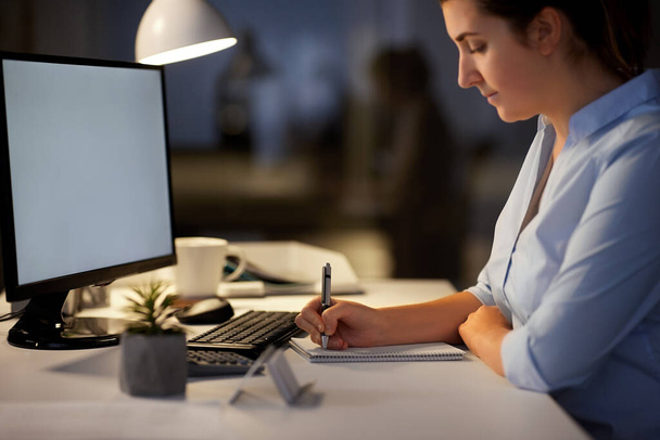 businesswoman writing to notebook at night office - Foto, Bild