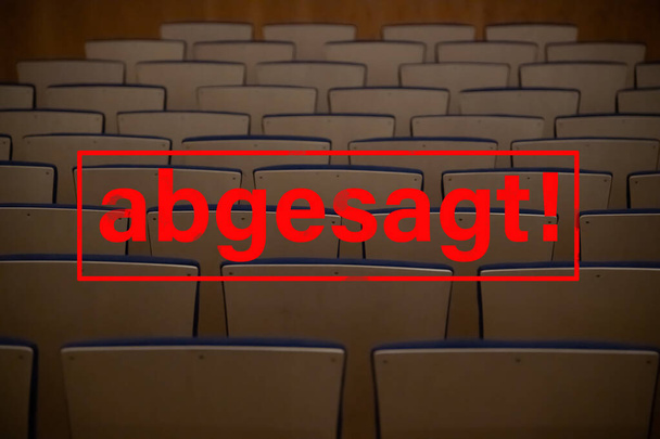 Rode stempel Duitse letters "abgesagt" betekent "geannuleerd" op lege stoelen in een concertzaal, bioscopen - Foto, afbeelding