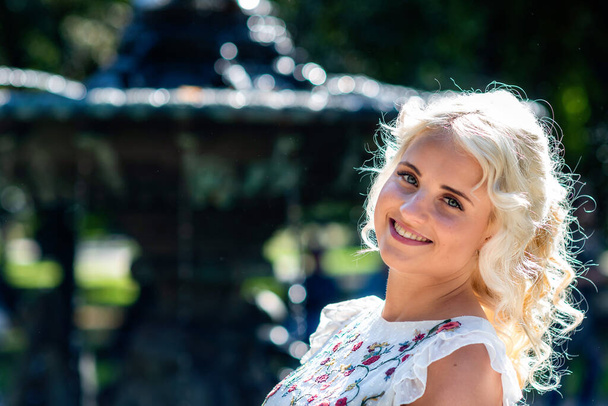 portret van een jonge, lachende, blonde vrouw met een wazige fontein op de achtergrond - Foto, afbeelding