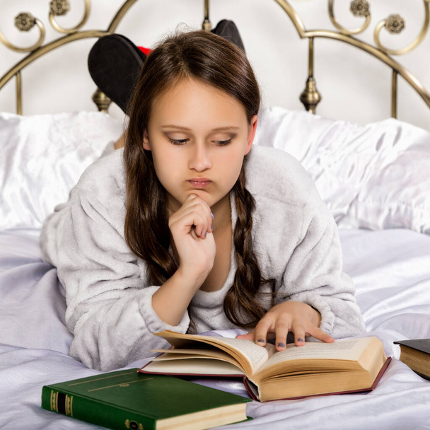sad young student girl reads a book while lying on a bed doing homework - Fotoğraf, Görsel