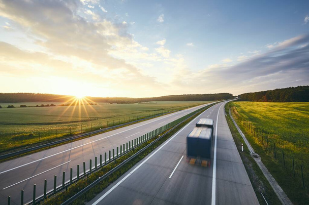 Wazige beweging van de truck. Verkeer op de snelweg in het midden van velden bij stralende zonsopgang.  - Foto, afbeelding
