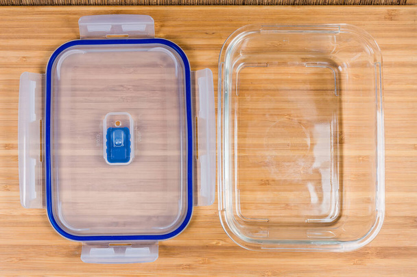 Leeres Glas, rechteckig belüfteter Vorratsbehälter für Lebensmittel und sein transluzenter Kunststoffdeckel daneben auf einer Holzoberfläche, Draufsicht - Foto, Bild