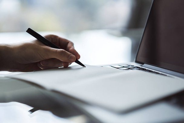 O homem escreve com uma caneta no caderno no teclado de computador portátil em um escritório ensolarado, negócio e conceito de educação. Fechar
 - Foto, Imagem