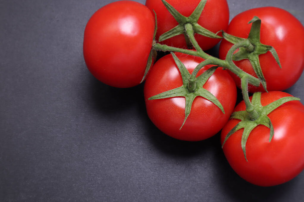 Tomates rojos maduros en una rama. Verduras sobre fondo negro texturizado
. - Foto, Imagen