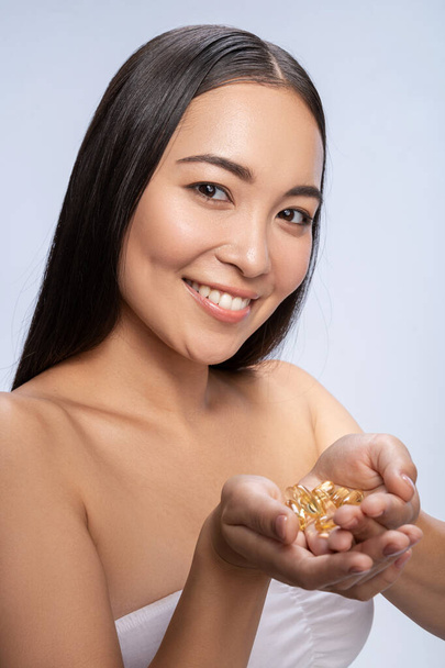 Happy Asian woman is taking tablets in studio - Fotografie, Obrázek