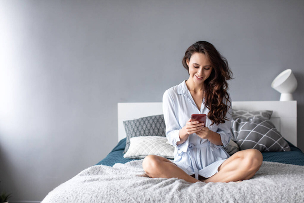 Smiling woman with phone on the bed. Use mobile internet at home. - Foto, imagen