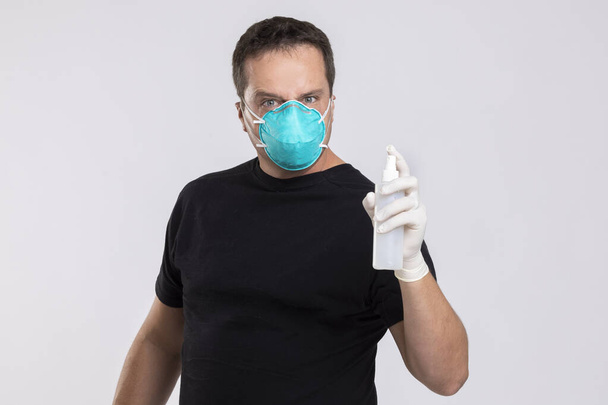 Man with a surgical mask holding up a bottle of disinfectant spray. - Photo, Image