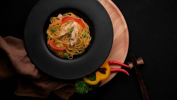 Top view of Schezwan Noodles or Chow Mein with vegetable, chicken and chilli sauce served in black plate - Foto, Imagen