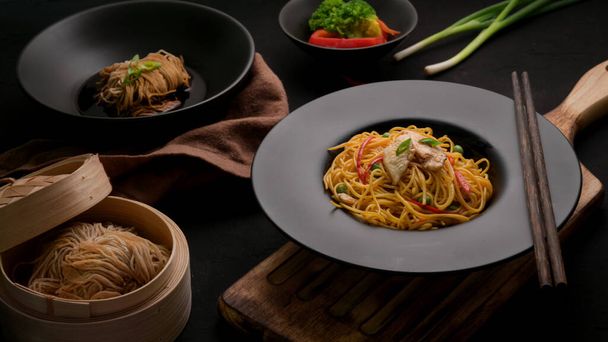 Foto recortada de fideos Schezwan o Chow Mein con salsa de verduras, pollo y chile servida en plato negro sobre mesa negra en restaurante chino
 - Foto, Imagen