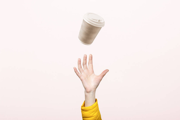χέρι πιάνει ένα γυαλί από χαρτόνι σε ένα ελαφρύ φόντο από χαρτόνι. Έννοια του καφέ, τσάι, διαφήμιση, διαλείμματα για καφέ. - Φωτογραφία, εικόνα