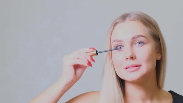 Pretty blond woman applying mascara make-up on her eyelashes in front of mirror. Beauty and makeup concept - Footage, Video