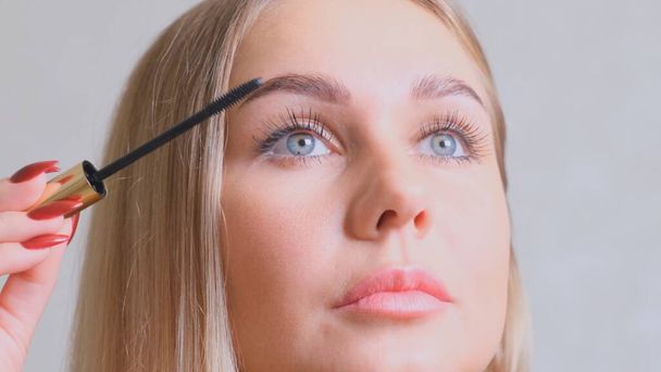 Confident happy young woman holding mascara apply on eyeleashes prepare getting ready in the morning, smiling beautiful girl doing make up put cosmetics on face looking in mirror in bathroom at home. - Photo, Image